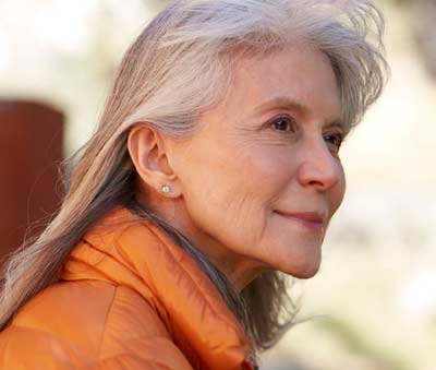 Older woman in an orange coat looking off into the distance