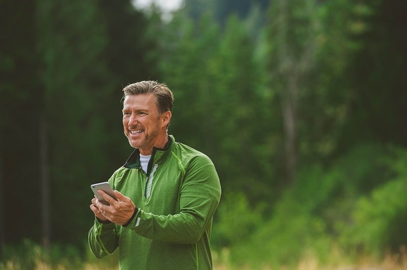 Man in a green shirt smiling on a walk while holding his phone