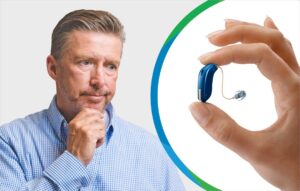 Middle aged man thinking and a behind the ear hearing aid in between a person's thumb and pointer finger