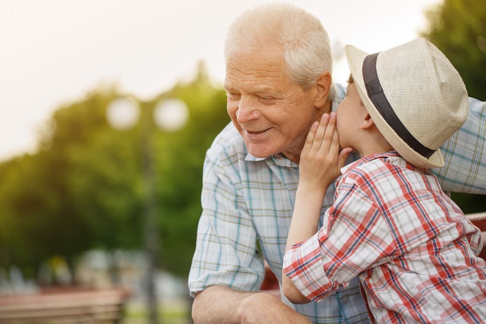 Young boy whispering into an elderly man's ear