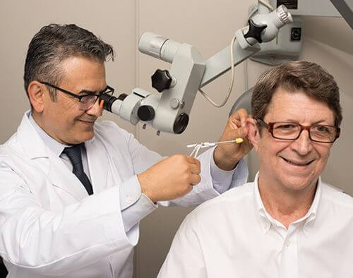 Audiologist inserting a Phonak Lyric Hearing aid into a middle aged man's ear